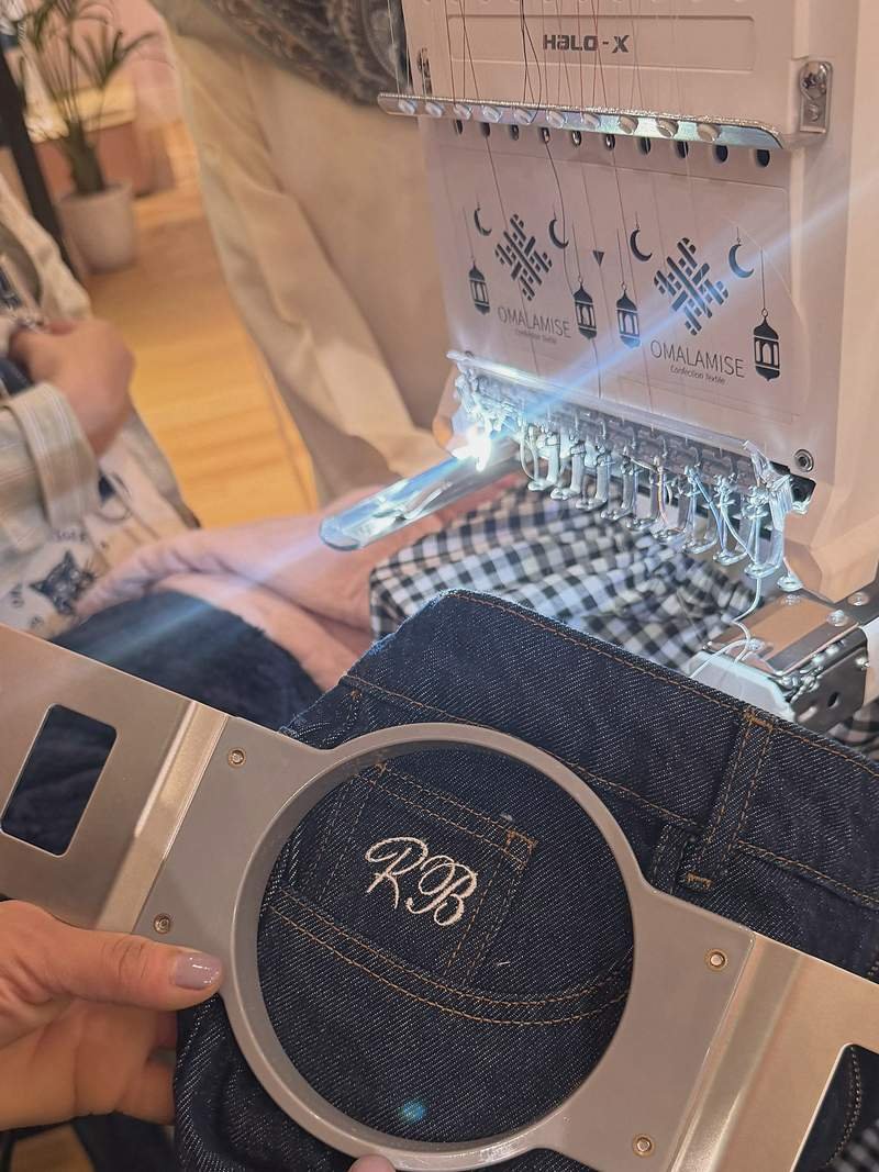 Cadre de broderie tenu en main devant la brodeuse, initiales RB brodées sur une poche de jean