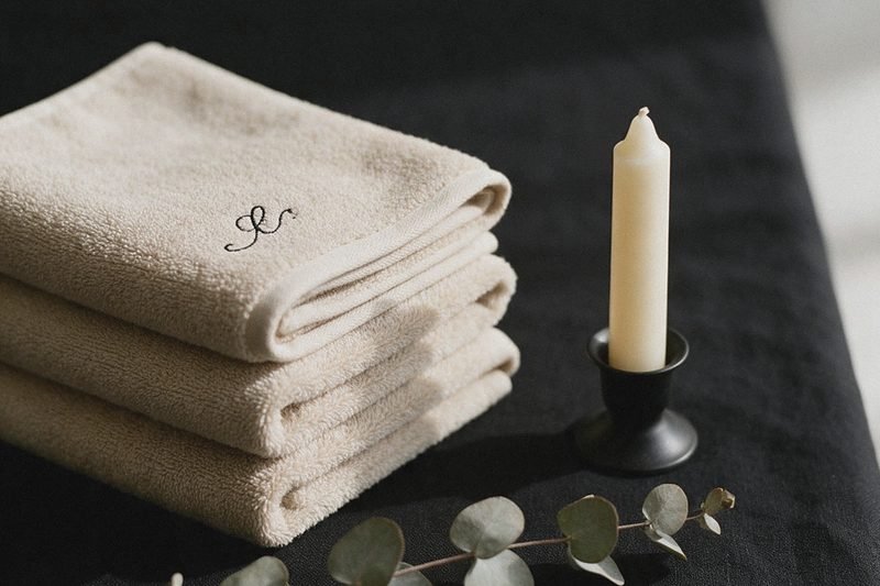 Trois serviettes beige pliées et brodées d'un monogramme, bougie crème sur nappe noire
